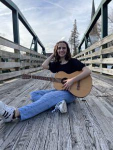 Student poet Hannah Camiolo sitting on bridge with guitar