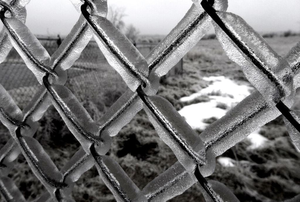 黑白照片的冰覆盖的栅栏与斑驳的雪在背景